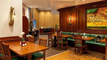 Ein Hotel-Essbereich mit Holztischen und grün gepolsterten Sitzgelegenheiten, eine Bar mit einem Leopardenbild und einem dekorativen Wandkunstwerk.