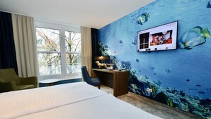 Ein Hotelzimmer mit Bett, Schreibtisch, Stuhl, Fernseher und einem großen Fenster.