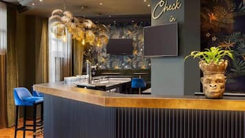 Una zona de bar con mostrador, taburetes, una pantalla de televisión y una planta decorativa.