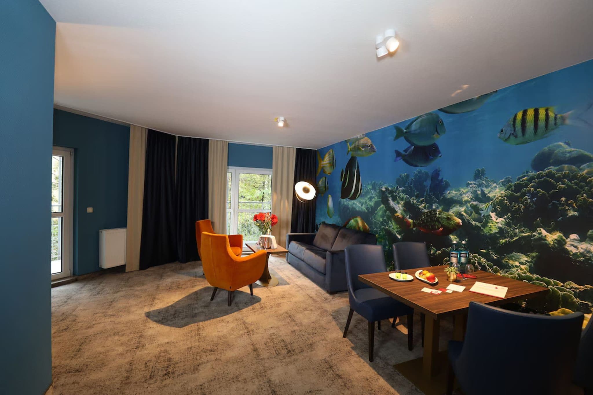 Een kamer met een groot wanddecoratie van een aquarium, een bank, een eettafel met stoelen, en een raam met gordijnen.