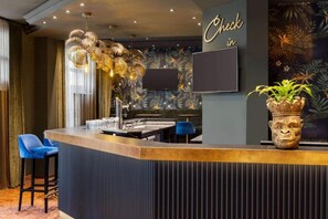 A bar area with a check-in sign, a flat-screen TV, and a decorative plant. - Sunday Hotel & Suites Leipzig - Suite Plus (Leipzig)
