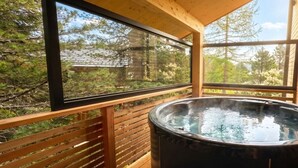 Um deck de madeira com hidromassagem, grandes janelas e vista para árvores.