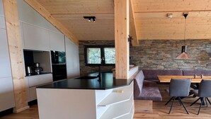 Cozinha moderna com ilha central, teto de madeira, parede de pedra e área de jantar com cadeiras e mesa.