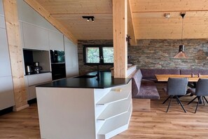 Eine moderne Küche mit einer zentralen Kochinsel, Holzboden, Steinwand und einem Essbereich mit Stühlen und Tisch.