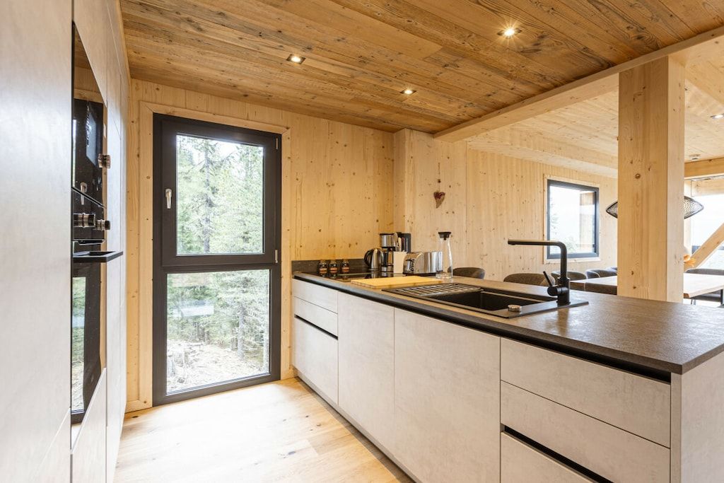 A modern kitchen with wooden cabinetry, a black countertop, and a large window.