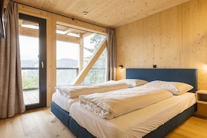 Ein Schlafzimmer mit zwei Betten, Holzboden, einer Schiebeglasdoor und Blick ins Freie.