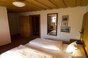 Un dormitorio con dos camas, vigas de madera en el techo, un espejo y cuadros enmarcados en la pared.