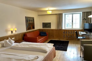 Ein Hotelzimmer mit einem Bett, einem roten Sofa, einem Schreibtisch mit Stuhl, einem Fernseher und einem Fenster mit Vorhängen.