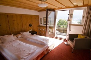 A bedroom with a large bed, a wooden headboard, a sofa, and a view through a sliding glass door. - Holiday apartment with 1 bedroom (Telfes)