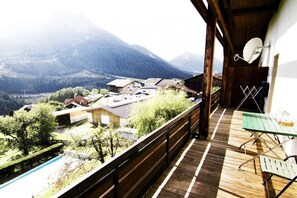 Terraza de madera con vistas a un paisaje montañoso, una antena parabólica y una mesa con sillas.