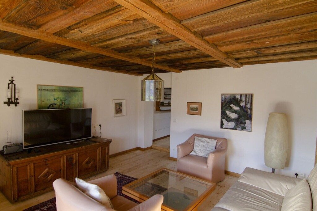 Una sala de estar con techo de madera, un televisor sobre un mueble de madera, un sofá, una mesa de centro de vidrio y una lámpara.