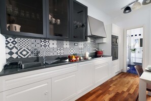 A modern kitchen with white cabinetry, a black countertop, and patterned backsplash. - Estate4home - Aranci 33 Guest House (Sorrento)