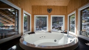 A spa room with a large oval hot tub, wooden walls, and large windows offering views of a snowy landscape. - Cabin in Turrach with sauna and balcony (Turrach)