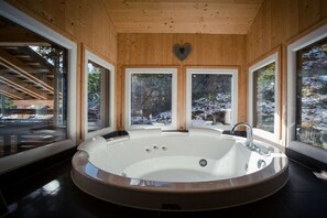 Spa-huone, jossa on suuri soikean muotoinen poreallas, puuseinät ja suuret ikkunat, joista avautuu näkymä lumiseen maisemaan.