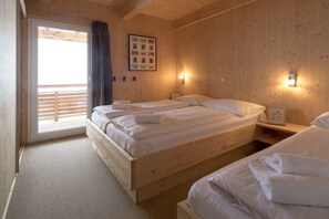 Ein Zimmer mit Holzboden, zwei Betten, einem Fenster mit Jalousien und einem an der Wand hängenden Bild.