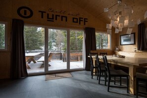 Ein Holzinnenraum mit einem großen Tisch und Stühlen, einem Schild mit der Aufschrift 'Chill out TURN OFF' und Blick auf eine Terrassenanlage.