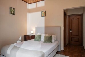 A bedroom with a bed, a nightstand, a lamp, and a door. - Vrbo Property (São Jorge)