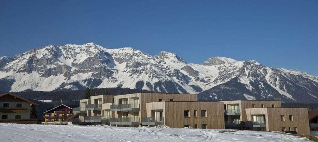Een modern gebouw met een plat dak en grote ramen, gelegen in een besneeerd landschap met bergen op de achtergrond.