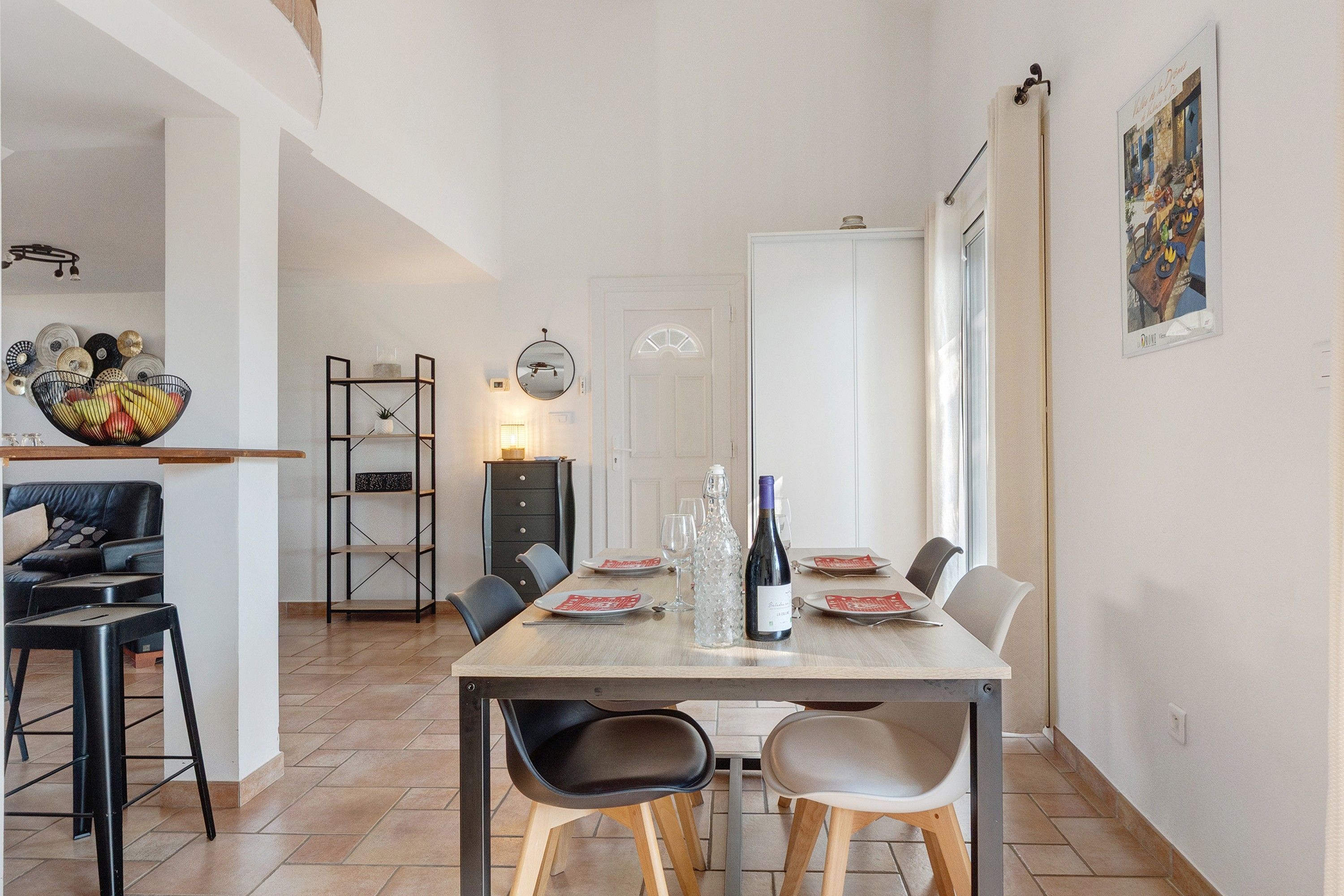 Un coin repas avec une table dressée pour deux personnes, une bouteille de vin et un bol décoratif placé à gauche.