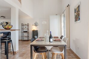 A dining area with a table set for two, a wine bottle, and a decorative bowl on the left.