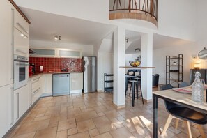 A modern kitchen with a built-in oven, a refrigerator, and a dishwasher. There is a dining area with a table and chairs, and a kitchen island with stools.