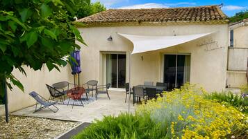 Un patio con mobiliario exterior, una zona de estar cubierta y un jardín con flores amarillas.