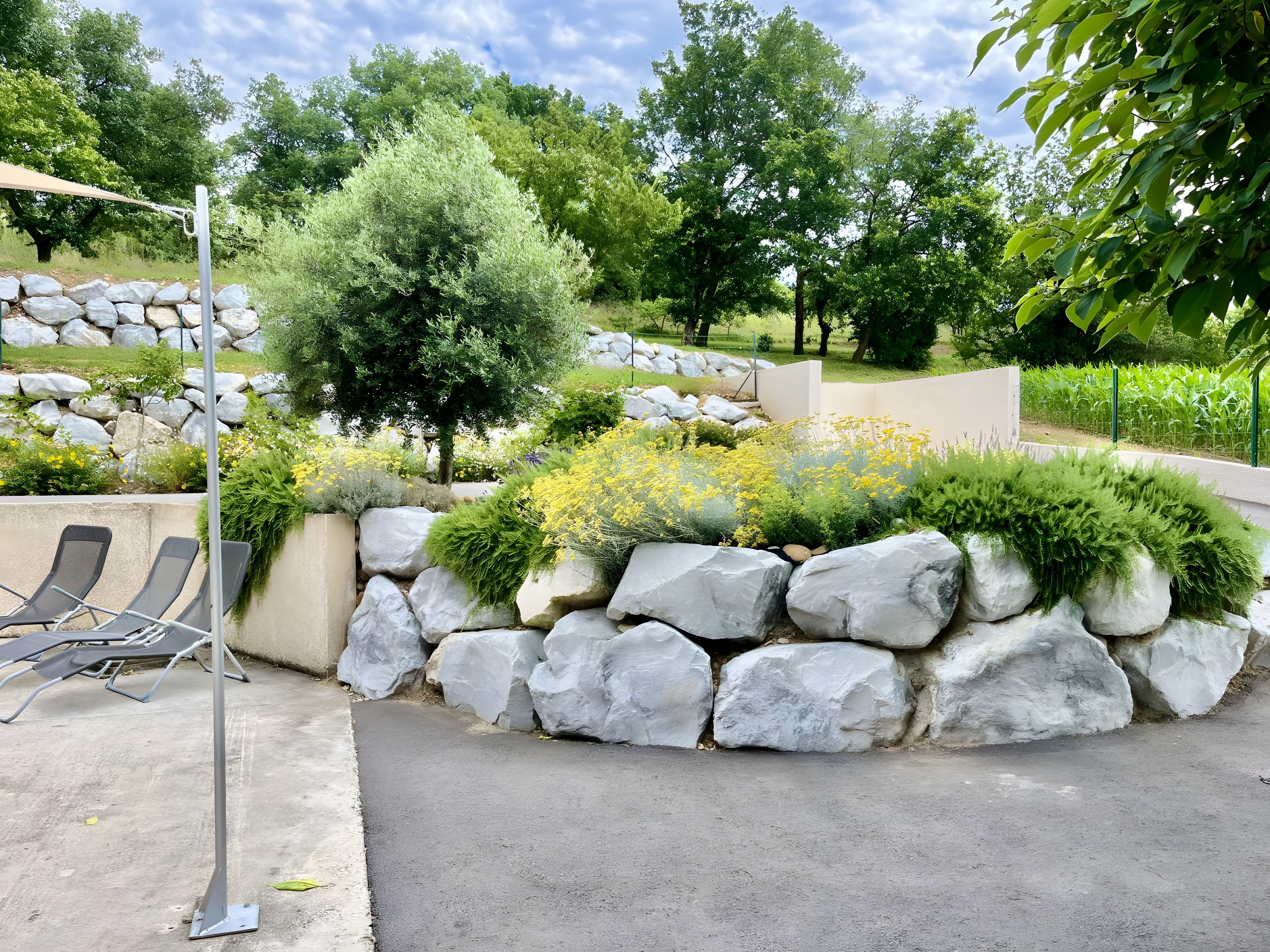 Ein angelegter Garten mit einer Steinmauer, gelben Blumen und einer Reihe von Liegestühlen.