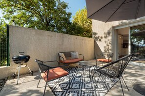 An outdoor patio with a grill, two chairs, and a patterned rug.