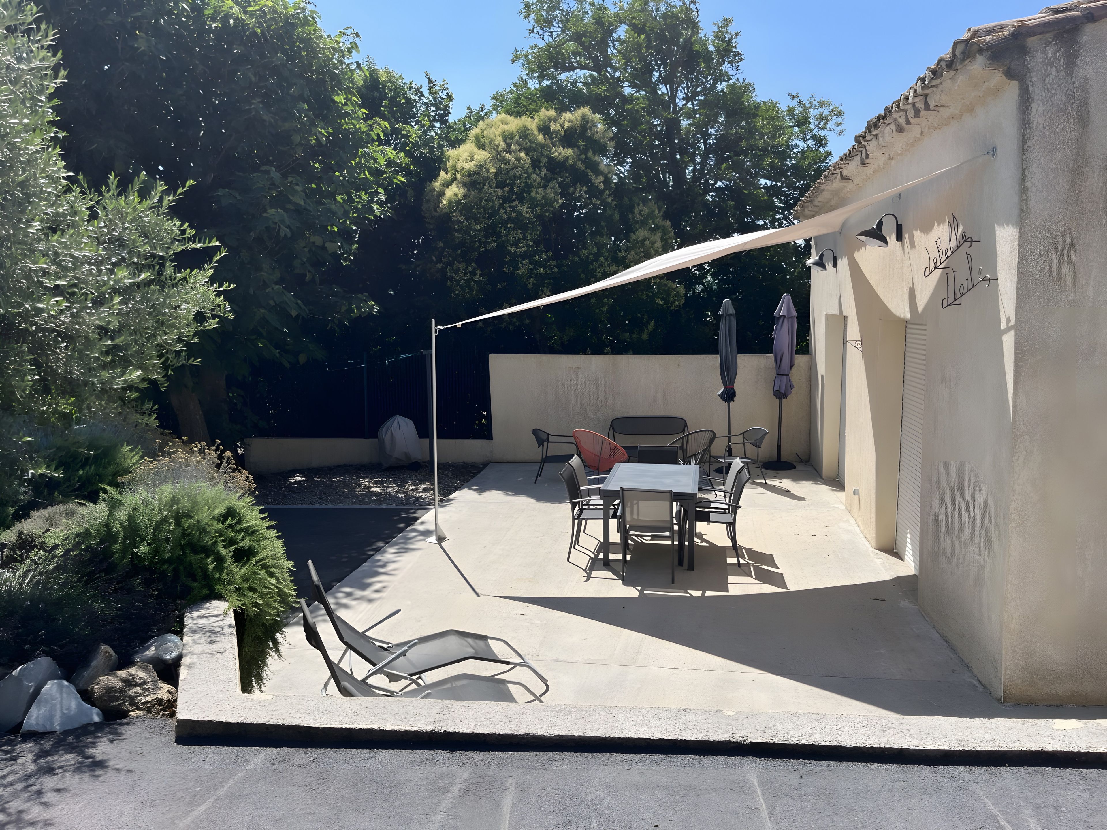 Un patio exterior con mesa y sillas, un área de estar cubierta y una pérgola que ofrece sombra.