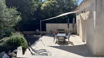 Un patio exterior con mesa y sillas, un área de estar cubierta y una pérgola que ofrece sombra.
