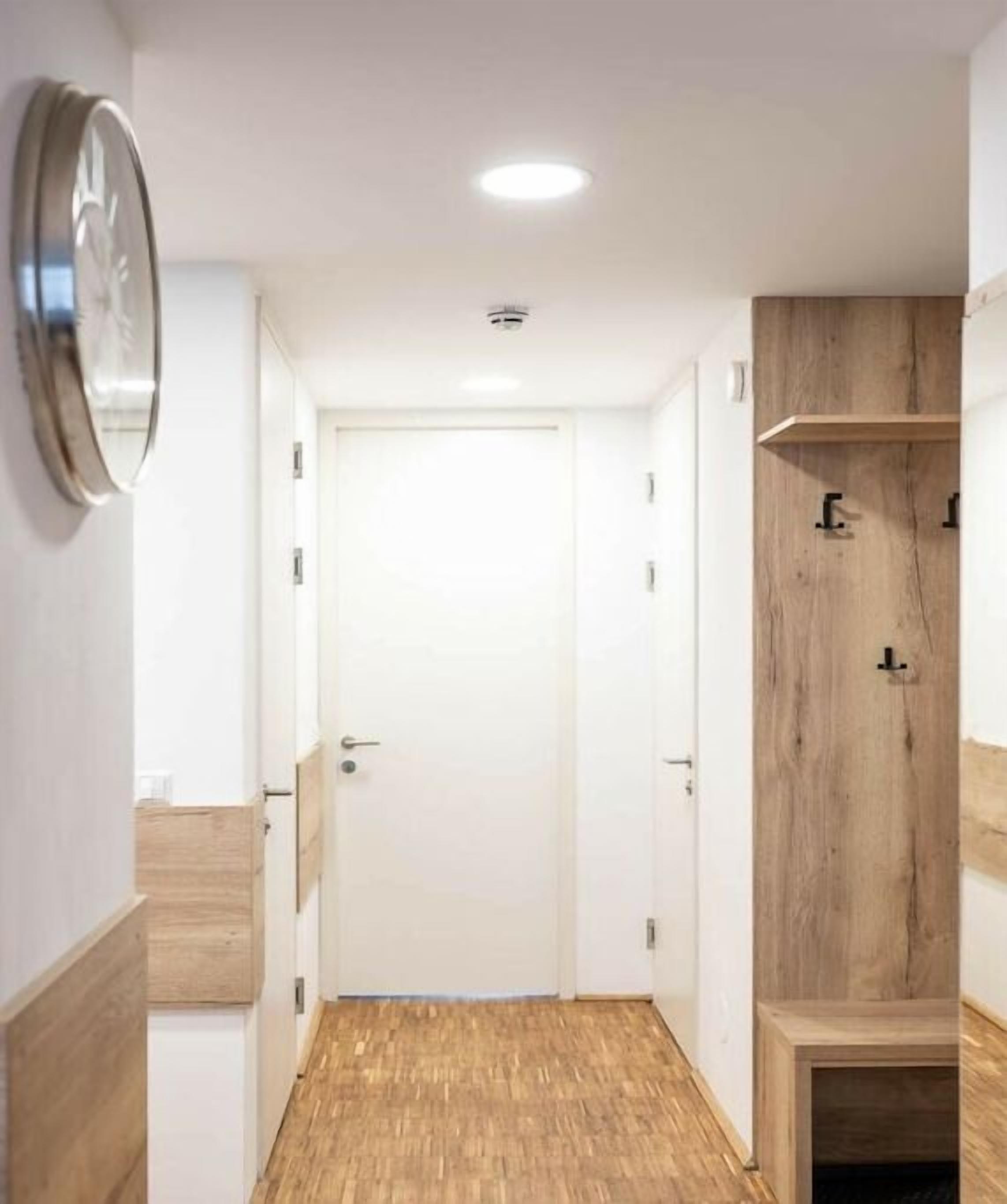 Een gang met een houten vloer, een witte deur aan het einde en een houten kast met een plank.