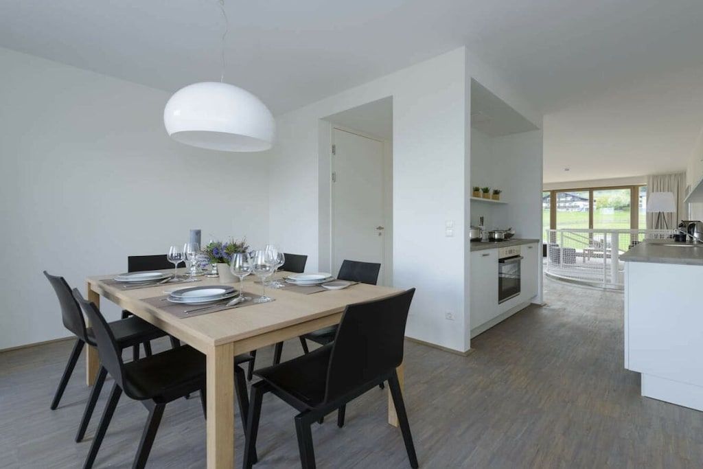 Een moderne eetruimte met een houten tafel voor vier personen, zwarte stoelen en een witte hanglamp.