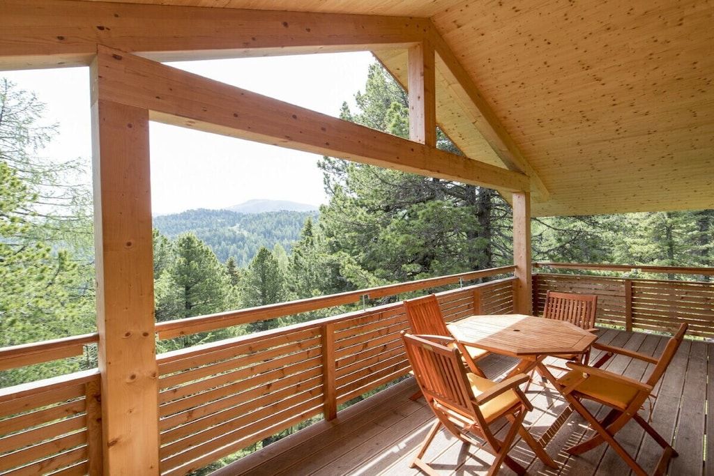Eine Holzterrasse mit Tisch und Stühlen mit Blick auf eine bewaldete Berglandschaft.