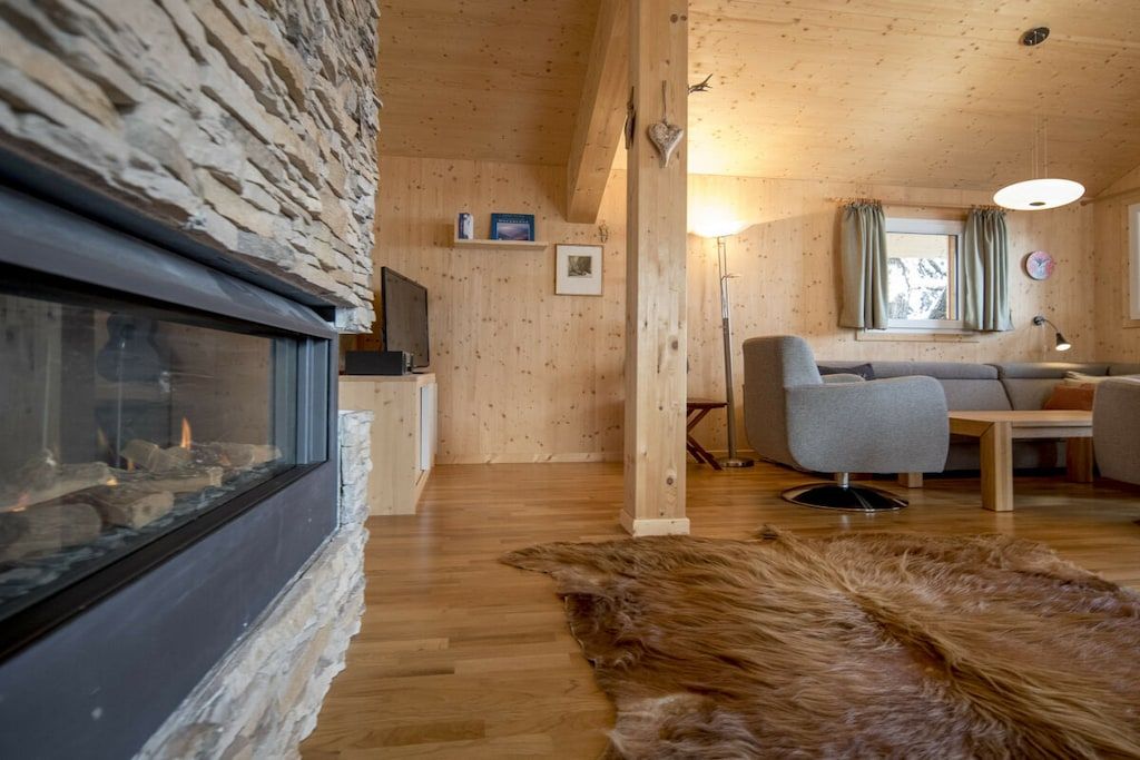 Un intérieur de chalet chaleureux avec un mur en pierre, une cheminée, un canapé et un tapis en fourrure.