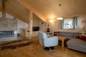 A cozy living room with a stone fireplace, a grey sofa, a wooden coffee table, and a television. - Cabin in Turrach with sauna and balcony (Turrach)