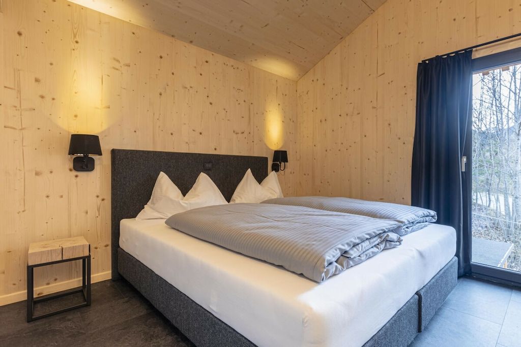 Une chambre à coucher avec un grand lit, deux lampes de chevet, une petite table et une fenêtre avec des rideaux.