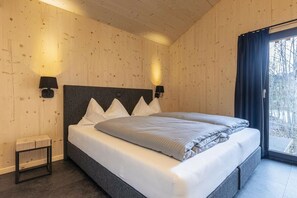 Ein Schlafzimmer mit einem großen Bett, zwei Nachttischlampen, einem kleinen Tisch und einem Fenster mit Vorhängen.
