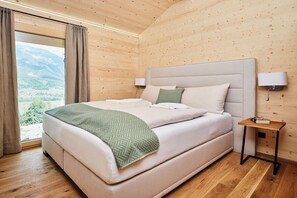Quarto com cama, mesa de cabeceira, luminária e janela com cortinas.