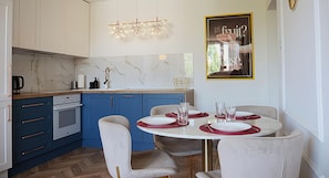 A modern kitchen with blue cabinets, a white countertop, and a dining area with a round table and four chairs. - Shipyard Apartments by Apartmore (GdaĆsk)