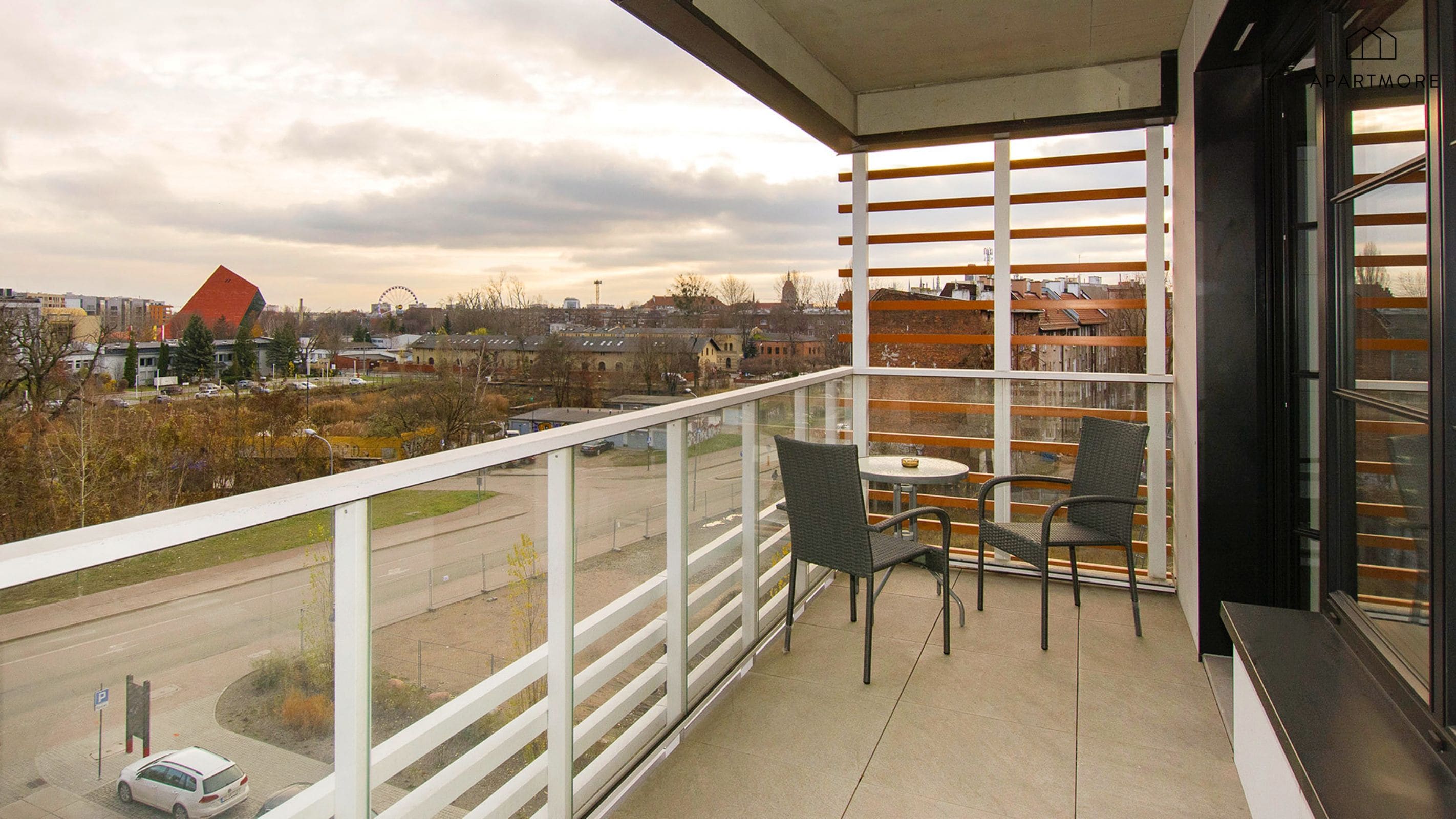 Een balkon met uitzicht op een stadsgezicht, inclusief een reuzenrad, en een tafel met stoelen.