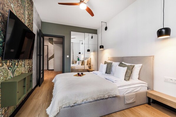 Un dormitorio moderno con una cama grande, un ventilador de techo, un televisor montado en la pared y un espejo que refleja la habitación.
