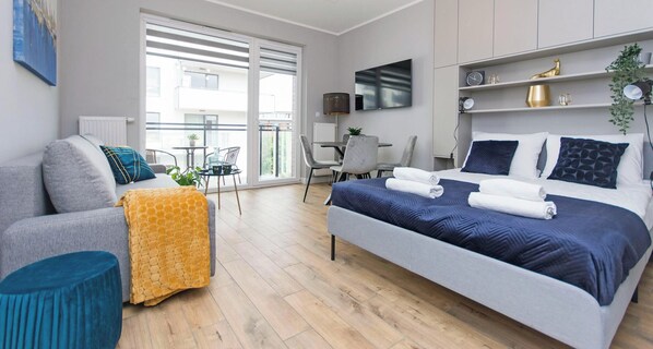 A modern hotel room with a bed, a sofa, a small table, and a balcony with a view. - Shipyard Apartments by Apartmore (Gdańsk)
