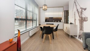 A compact living space with a dining area, kitchenette, and a view of the cityscape through large windows. - Shipyard Apartments by Apartmore (Gdańsk)
