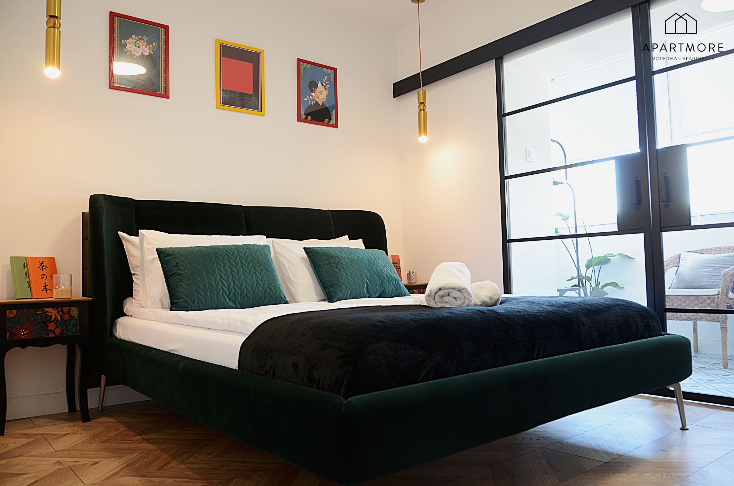 A modern bedroom with a dark green bed, white bedding, and a large window providing a view of the outside.