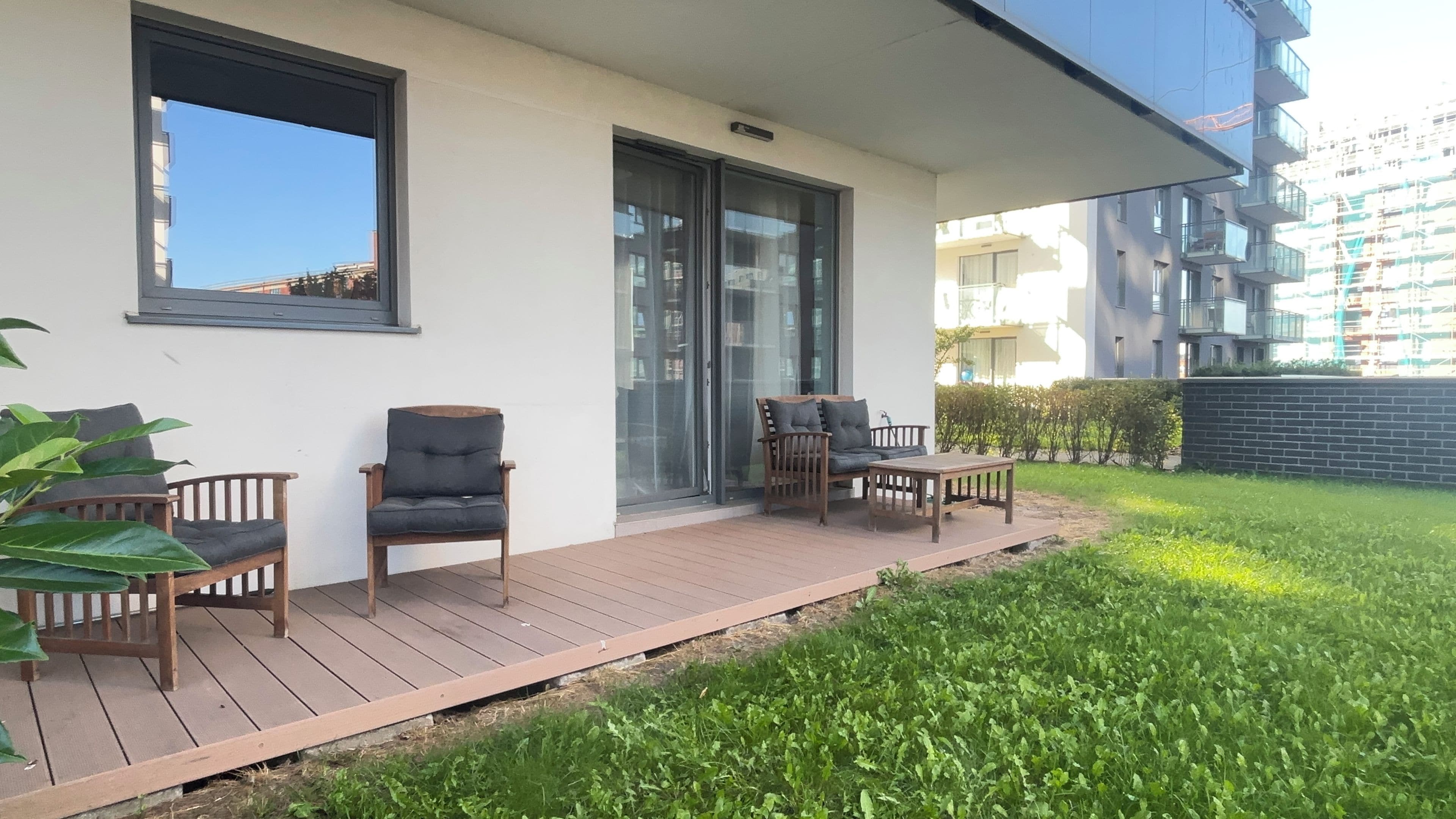 Ein moderner Außenbereich zum Sitzen mit einer Holzterrasse, zwei Stühlen und einem Tisch.