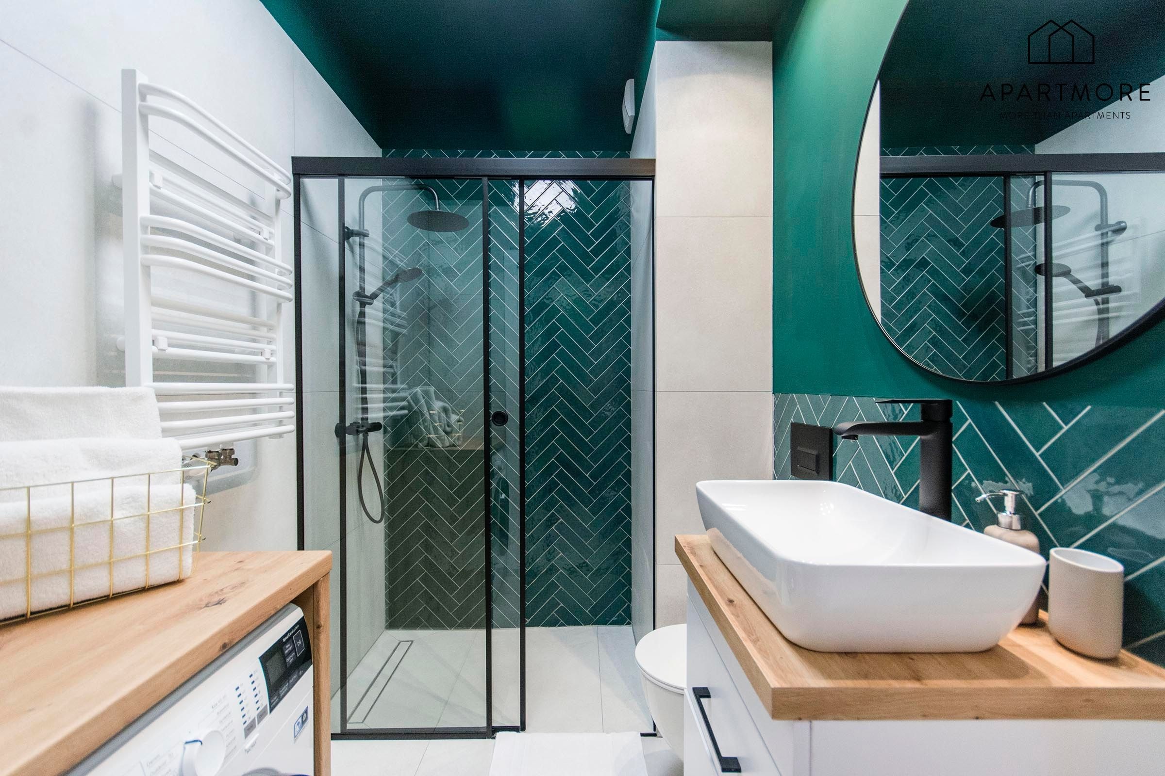 A modern bathroom with a glass-enclosed shower, a white sink, and a mirror with a herringbone tile backsplash.
