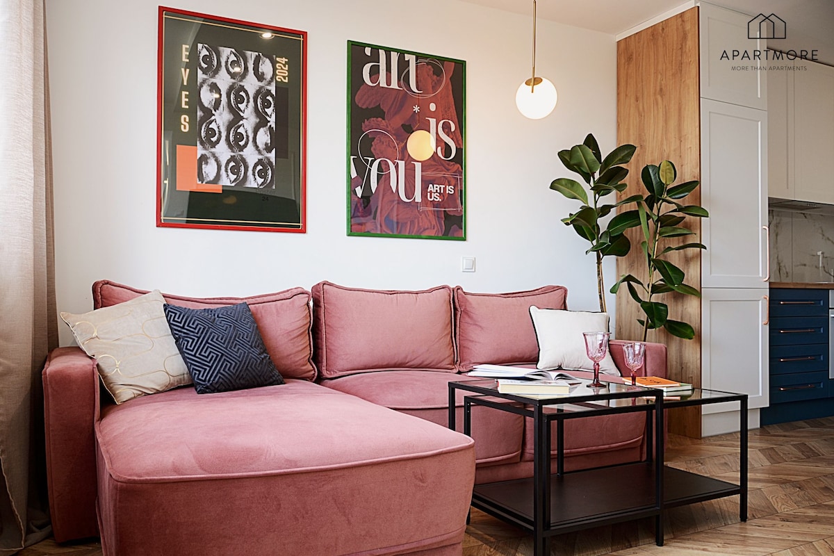 Ein modernes Wohnzimmer mit einem rosafarbenen Sofa, einem Glastisch und zwei gerahmten Kunstwerken an der Wand.