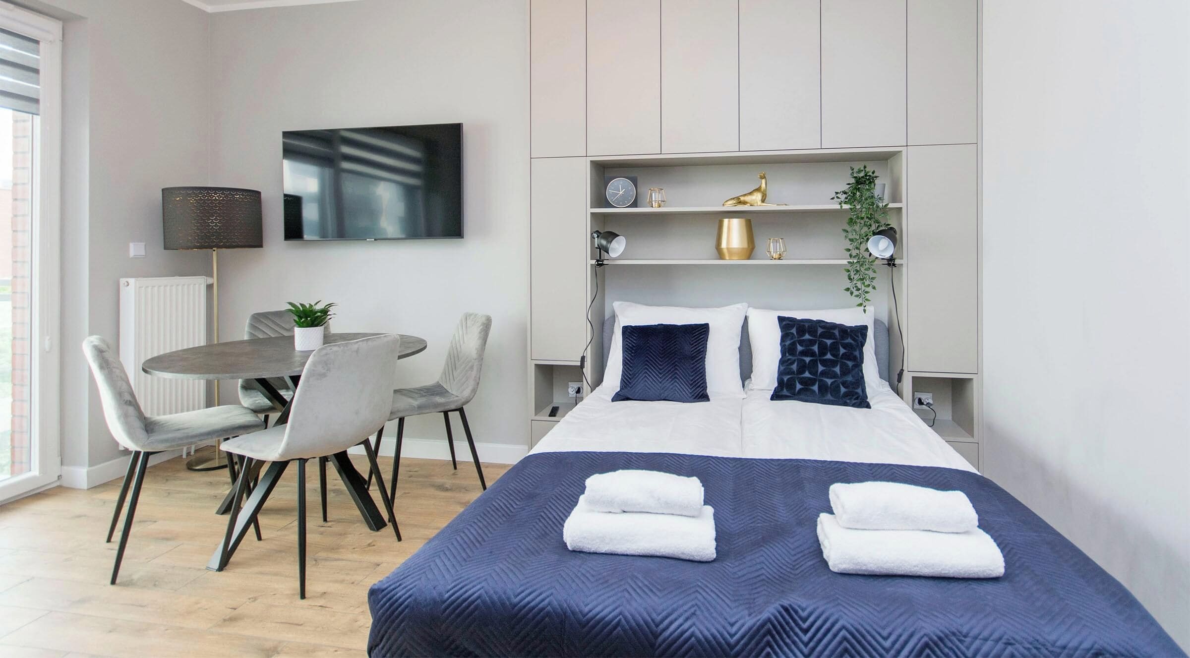 Ein modernes Hotelzimmer mit Bett, Nachttischen, einem Schreibtisch, Stühlen, einem Fernseher und einer Pflanze.