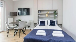 Habitación de hotel moderna con cama, mesitas de noche, escritorio, sillas, televisor y planta.