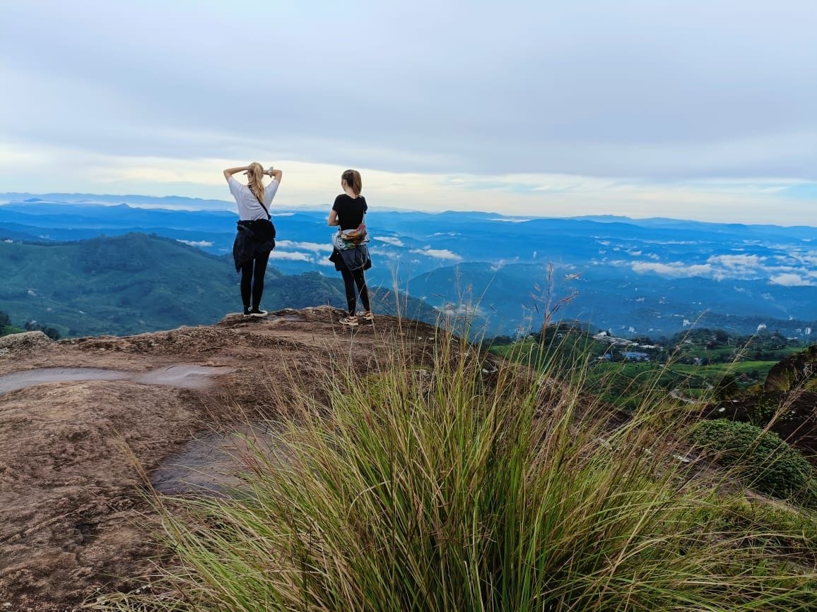 Duas pessoas em um afloramento rochoso com vista para uma paisagem montanhosa.